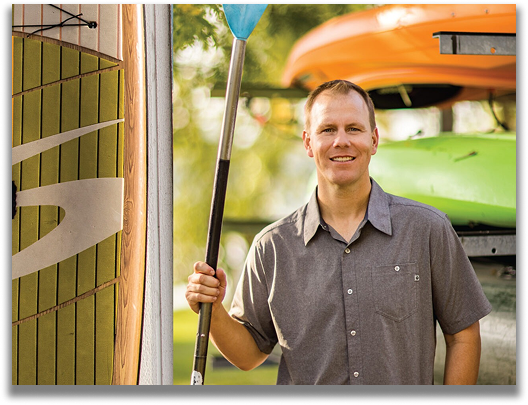 Tyler Leeper holding an oar standing by a rack of canoes